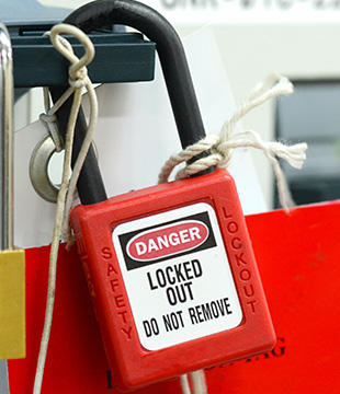 a red lock reading DANGER Locked Out Do Not Remove hangs clipped to a switch. The lock has name tags hanging from it.